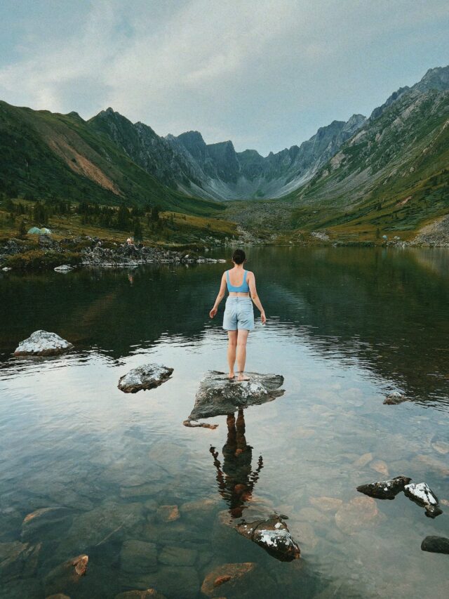 free-photo-of-back-view-of-a-woman-standing-on-a-rock-in-a-mountain-lake